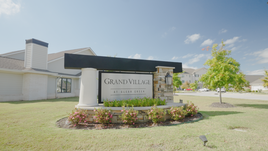 A sign in front of a luxury retirement community reads "Grand Village at Clear Creek".
