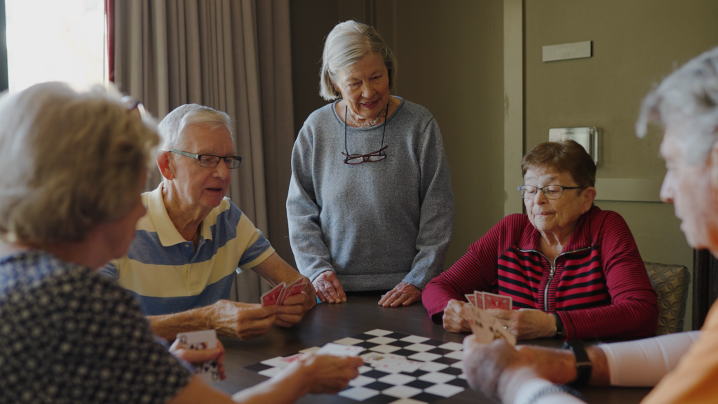 A group of retirees smiles and plays cards around a table.