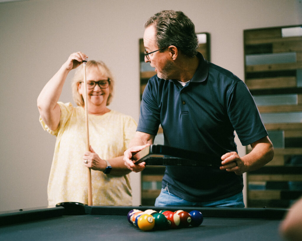 A man and a woman rack up pool balls and dust their cues in the recreation area at Grand Village, an independent living retirement community in Fayetteville, Arkansas.