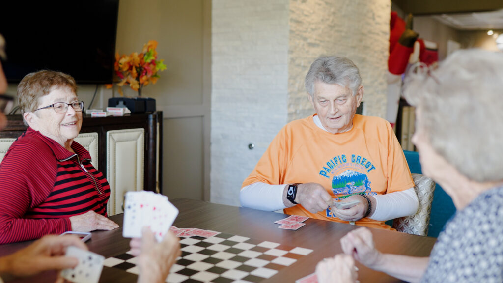 A group of smiling senior adults plays a competitive card game at Grand Village, an independent living retirement community in Fayetteville, Arkansas.
