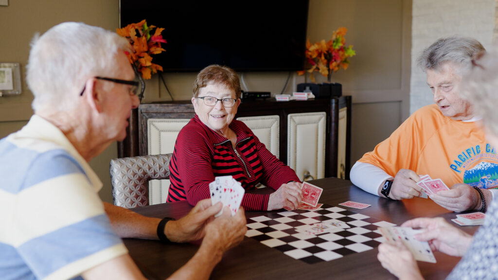 A group of smiling retirees enjoy playing cards while laughing and joking.