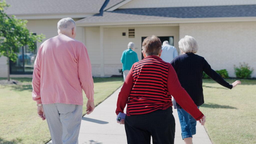 A group of retirees walk freely and happily across the grounds of an independent living community.